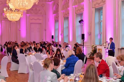 Annegret Kramp-Karrenbauer steht in einem pink beleuchteten Saal an einem Rednerpult. Im Publikum sitzen Frauen auf weißen Stühlen.