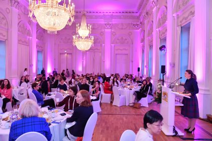 Digitalministerin Judith Gerlach steht in einem pink beleuchteten Saal an einem Rednerpult. Im Publikum sitzen Frauen auf weißen Stühlen.