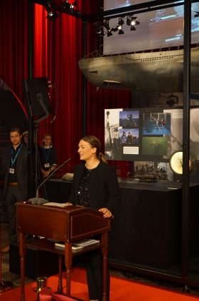 Digitalministerin Judith Gerlach steht vor einer Glasvitrine am Rednerpult, dahinter ein roter Vorhang.