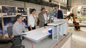 Digitalministerin Judith Gerlach lässt sich von Prof. Schilling in einer Maschinenhalle einen Roboterarm demonstrieren.