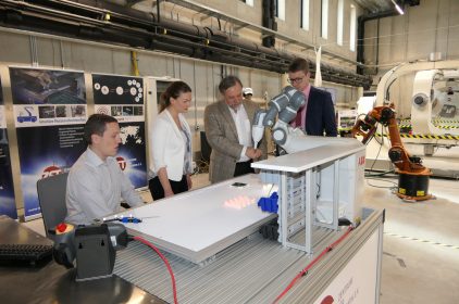 Digitalministerin Judith Gerlach lässt sich von Prof. Schilling in einer Maschinenhalle einen Roboterarm demonstrieren.