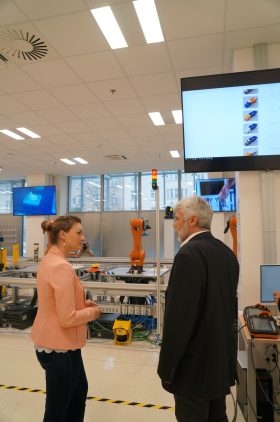 Digitalministerin Gerlach im Gespräch mit einem Mann, im Hintergrund sieht man Roboterteile.
