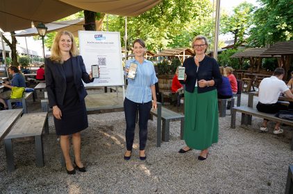 Digitalministerin und Schirmherrin Judith Gerlach, MdL (Mitte), AKDB-Vorstandsmitglied Gudrun Aschenbrenner und DEHOGA Bayern-Präsidentin Angela Inselkammer testen eine Registrierungs-App in einem Münchner Biergarten.