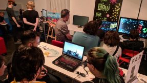 Die Teilnehmer der Games Bavaria Vernissage schätzen den kreativen Austausch mit Gleichgesinnten: Personen sitzen vor geöffneten Laptops und sprechen miteinander.