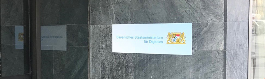 Außenfassade des Digitalministeriums. Rechts im Bild ist ein Schild mit der Aufschrift 'Bayerisches Staatsministerium für Digitales' zu sehen.
