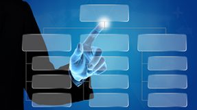 Ein transparentes Organigramm vor blauem Hintergrund und einer fokussierten Hand, die eines der Organigramm-Felder beruehrt.
