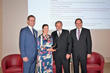 Gruppenbild mit Digitalministerin Judith Gerlach mit einem Mini-Satellit vor roten Sesseln.