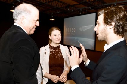 Digitalministerin Judith Gerlach im Gespräch mit zwei Herren. Im Hintergrund ist eine Leinwand zu mit der Aufschrift Rodeo zu sehen.