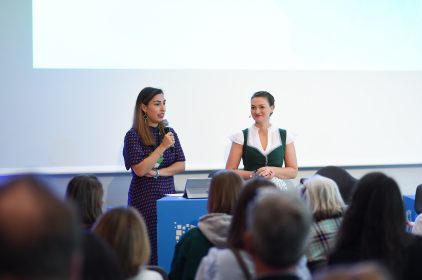 Digitalministerin Judith Gerlach im Dirndl. Daneben steht eine Frau mit Mikrophon.