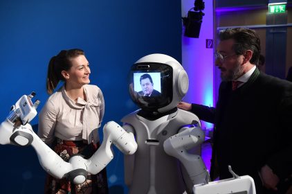 Digitalministerin Judith Gerlach, MdL, zusammen mit Prof. Dr.-Ing. Sami Haddadin und Franz Josef Strauß. Natürlich nicht dem Echten, sondern einem KI-Roboter, auf dessen Gesicht mit Hilfe von Morphing das Gesicht und die Stimme des 1988 verstorbenen Ministerpräsidenten erscheint. <br />
© StMD / Andreas Gebert<br />
