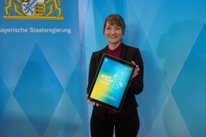 Digitalministerin Gerlach mit einem Tablet, auf dem 'Block.Chain.Trust' steht.