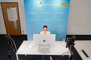 Digitalministerin Judith Gerlach sitzt vor einem PC an einem Schreibtisch. Im Hintergrund ist eine Pressestellwand des Bayerischen Staatsministeriums für Digitales aufgebaut.
