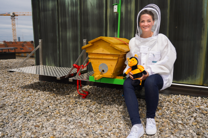 Digitalministerin Judith Gerlach sitzt im Imkeranzug auf dem Dach des Digitalministeriums neben dem Hightech-Bienenstock.