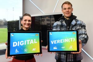 Digitalministerin Gerlach und Welttorhüter Manuel Neuer halten Tablets in die Kamera. Darauf steht: Digital Verein(t)