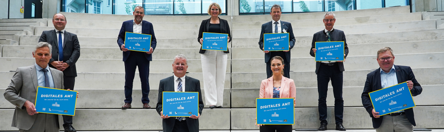Digitalministerin Judith Gerlach (vorne), die Augsburger Oberbürgermeisterin Eva Weber und fünf Herren halten jeweils ein Schild mit der Aufschrift 'Digitales Amt' hoch. Gruppenbild zur Initiative Digitales Amt