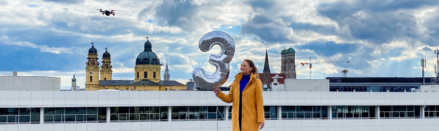 Frau steht in München auf einem Dach und hält einen Luftballon. Digitalministerin Judith Gerlach steht zum dreijährigen Jubiläum des Digitalministeriums auf dem Dach des Hauses und hält einen Luftballon.