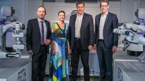 Gruppenbild von vier Personen. Im Hintergrund sind Roboter zu sehen.