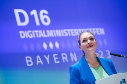 Digitalministerin Gerlach spricht in ein Mikrophon an einem Rednerpult. Im Hintergrund der Schriftzug: D16 Digitalministertreffen Bayern 2023.
