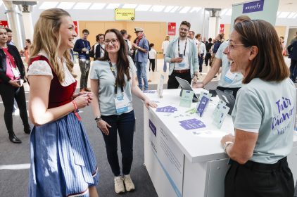 Digitalministerin Gerlach im Gespräch mit zwei Ausstellerinnen eines Startups an einem Stand auf der Bits & Pretzels 2023.