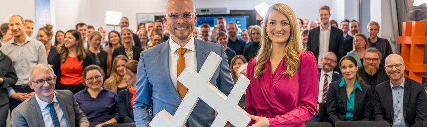 Digitalminister Dr. Fabian Mehring und die ehemalige Digitalministerin Judith Gerlach halten ein Hashtag-Zeichen in den Händen. Im Hintergrund das Team des Digitalministeriums.