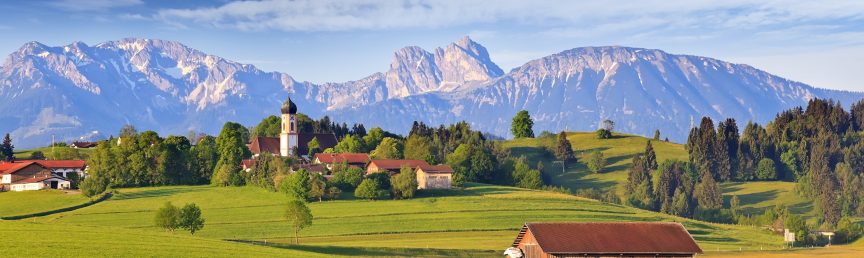 Gemeinde mit einer Kirche vor bayerischer Bergkulisse.